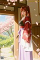 A woman in traditional attire stands by an open door, holding a sword, with cherry blossoms falling around her.