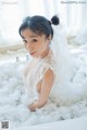 A woman in a white dress sitting in a bathtub covered in foam.