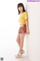 A young woman leaning against a white wall wearing a yellow shirt.