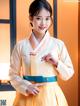 A woman in a yellow and blue hanbok poses for a picture.