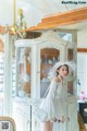 A woman in a white dress and hat standing in front of a cabinet.