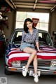 A woman sitting on top of a car covered in an American flag.